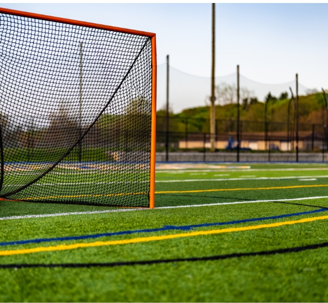 A lacrosse goal sits on an outdoor turf field with painted lines.
